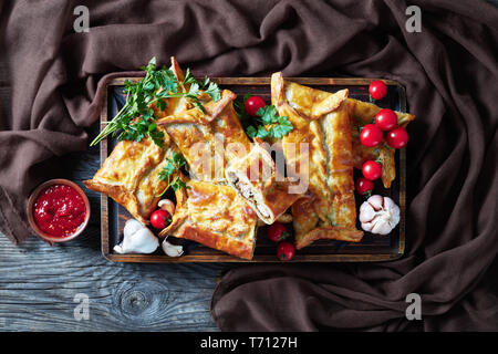 Chicken and ground walnut Stuffed Puff Pastry Borek,  Baked Chicken Pies, Puff Pastry Chicken Bundles on a cutting board with tomato salsa and parsley Stock Photo