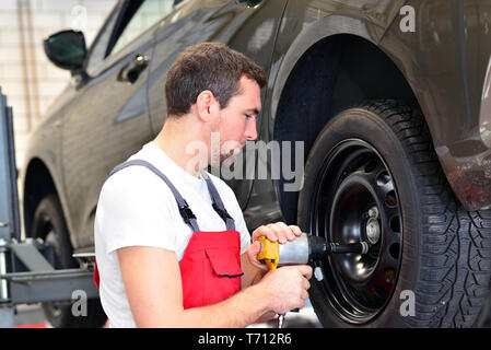 professional car mechanic works in a workshop and changes tyres on the vehicle Stock Photo