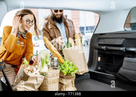 Young couple packing shopping bags with fresh food into the car trunk, view from the vehicle interior Stock Photo