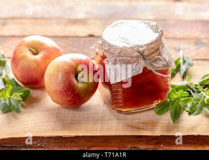 One full small glass jar closed with homemade paper lid with homemade apple jam and two whole apples and greem mint on wooden background. Natural home Stock Photo