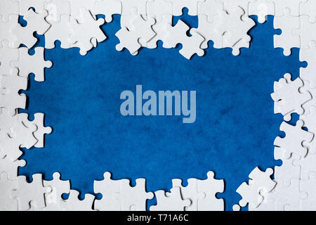 Framing in the form of a rectangle, made of a white jigsaw puzzle. Frame text and jigsaw puzzles. Frame made of jigsaw puzzle pieces on blue backgroun Stock Photo