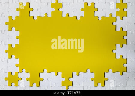 Framing in the form of a rectangle, made of a white jigsaw puzzle. Frame text and jigsaw puzzles. Frame made of jigsaw puzzle pieces on yellow backgro Stock Photo