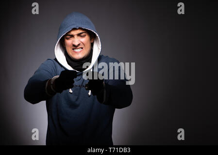 Young gangster in hood on grey background Stock Photo