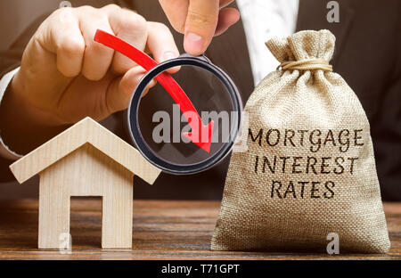 Bag with the money and the word Mortgage interest rates and arrow down and house. Low interest in mortgages. Reducing interest payments for mortgages. Stock Photo