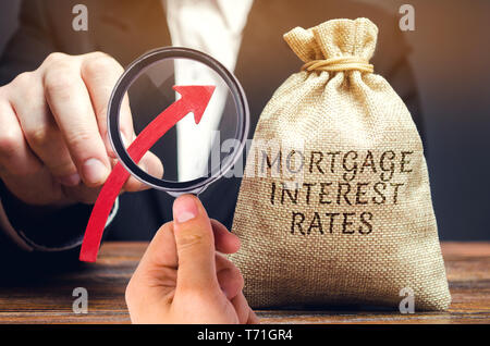 Bag with the money and the word Mortgage interest rates and up arrow in male hands. Raising mortgage rates and tax. The increase in interest charges.  Stock Photo