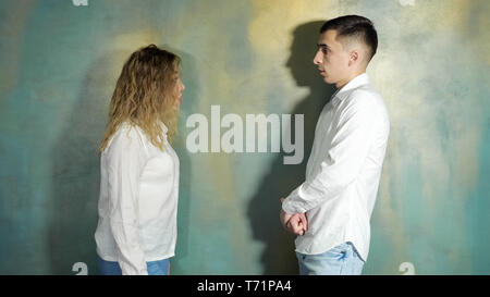 Young couple husband and wife are arguing and shouting each other standing near the wall, side view. Stock Photo