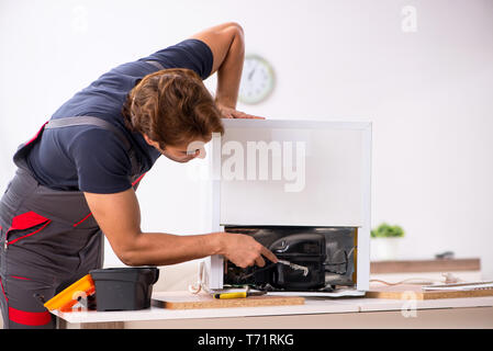 Young handsome contractor repairing fridge Stock Photo