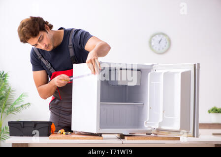 Young handsome contractor repairing fridge Stock Photo