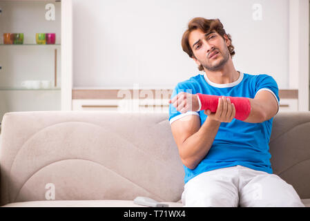 Young man with injured arm sitting on the sofa Stock Photo