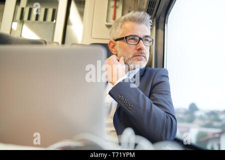 Businessman sitting in train, looking by window Stock Photo
