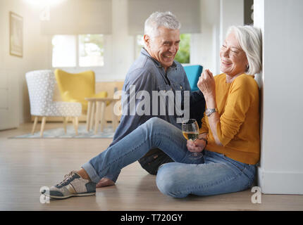Relaxed senior couple sitting on floor in modern home with glass of wine Stock Photo