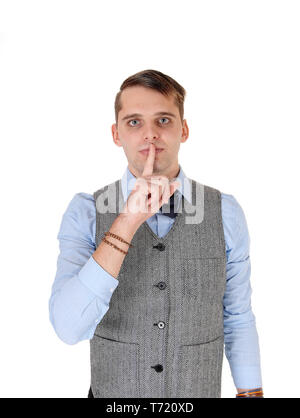 Young man in a vest standing with finger over mouth Stock Photo