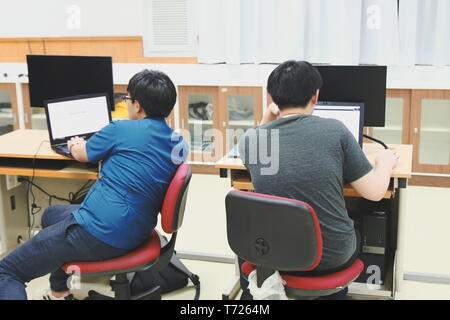 Two Thai Computer Engineering students at Assumption University (ABAC) working on their own laptop during class Stock Photo