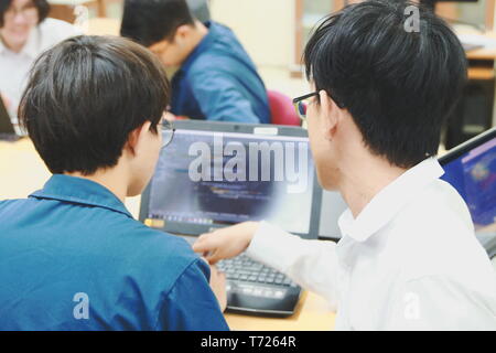 Two Thai computer engineering student discussing about the computer code in their project on a laptop during the class Stock Photo