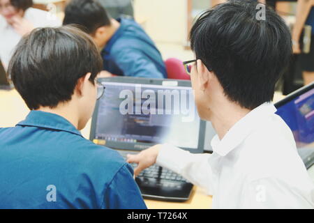 Two Thai computer engineering student discussing about the computer code in their project on a laptop during the class Stock Photo
