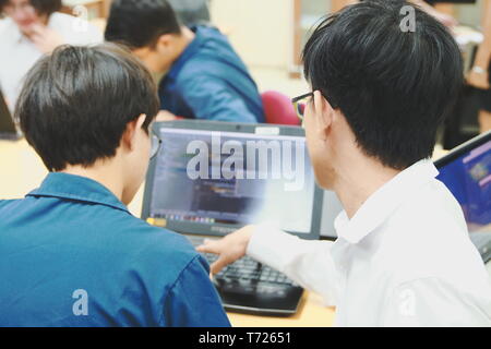 Two Thai computer engineering student discussing about the computer code in their project on a laptop during the class Stock Photo