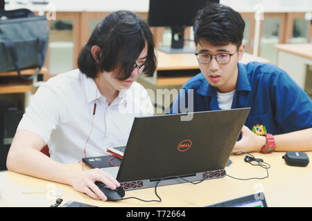 Two Chinese computer engineering student working together on a laptop in a computer programming class Stock Photo