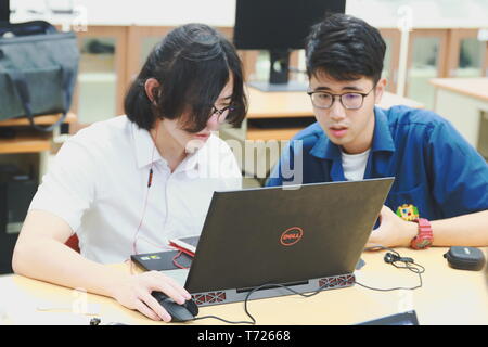 Two Chinese computer engineering student working together on a laptop in a computer programming class Stock Photo