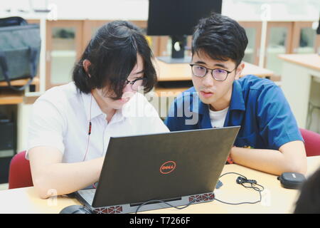 Two Chinese computer engineering student working together on a laptop in a computer programming class Stock Photo
