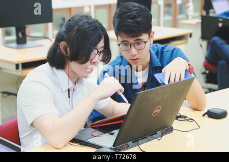 Two Chinese computer engineering student working together on a laptop in a computer programming class Stock Photo