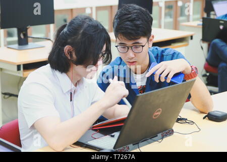 Two Chinese computer engineering student working together on a laptop in a computer programming class Stock Photo