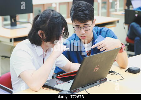 Two Chinese computer engineering student working together on a laptop in a computer programming class Stock Photo