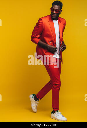 Full length of stylish young african man in orange outfit over yellow background. Fashion model in smart casuals. Stock Photo