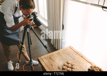 Female chef taking pictures of dessert on table with dslr camera mounted on tripod. Female taking pictures of sweet food for her blog. Stock Photo