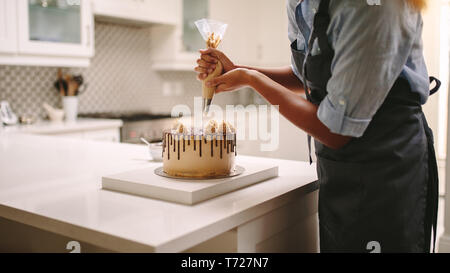 Female chef with pastry bag squeezing cream on cake at kitchen. Woman preparing a cake at home. Stock Photo