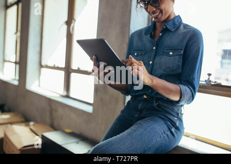 Female entrepreneur in office using digital tablet. Tablet computer hand of a woman wearing casuals sitting at window sill in office. Stock Photo