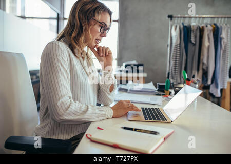 Businesswoman sitting at her desk and working on laptop. Dropshipping business owner looking for new orders on her laptop. Stock Photo