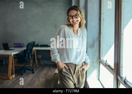 Successful female entrepreneur standing in office with hands in pocket. businesswoman in casuals standing near window in office. Stock Photo
