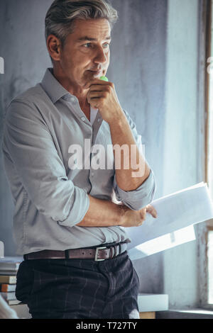 Mature businessman standing in office and thinking. businessman in casuals at his office looking pensive. Stock Photo