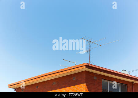Analogue tv antennas perched on top of red retro brick house. Stock Photo