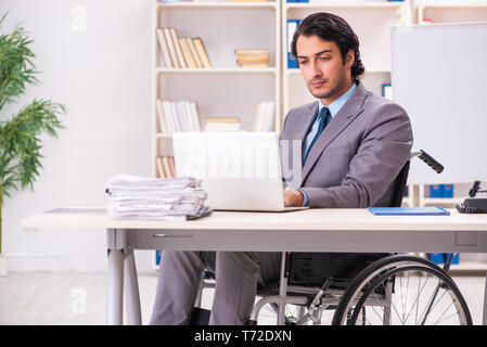 Young handsome employee in wheelchair at the office Stock Photo