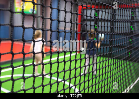 Blurred children are playing behind the net at indoor playground in activity park. Stock Photo