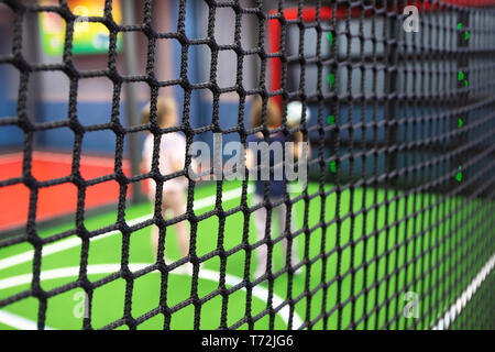 Blurred children are playing behind the net at indoor playground in activity park. Stock Photo