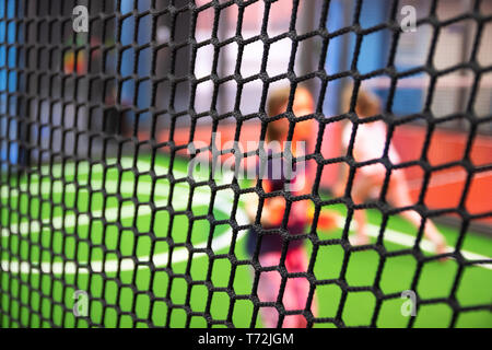 Blurred children are playing behind the net at indoor playground in activity park. Stock Photo