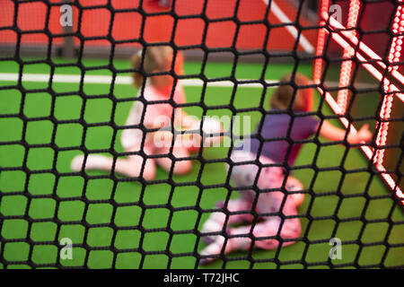 Blurred children are playing behind the net at indoor playground in activity park. Stock Photo