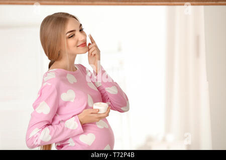 Young pregnant woman applying cream onto skin in bathroom Stock Photo