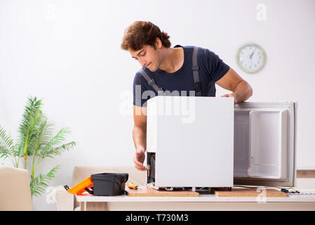 Young handsome contractor repairing fridge Stock Photo