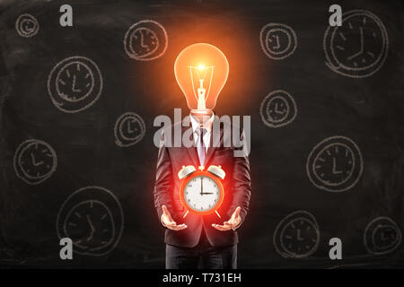 Man in suit with lightbulb instead head, levitating big red alarm clock above palms, standing against black wall with pattern of alarm clocks on it. Stock Photo