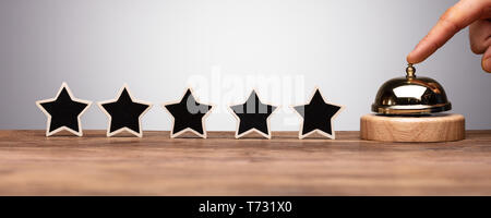 A Person's Hand Ringing Service Bell Near Black Five Star Rating Icon On Wooden Desk Stock Photo