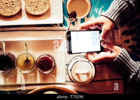 Breakfast morning and chat messages with mobile phone - people working with technology or addicted to internet - home or hotel travel lifestyle for mo Stock Photo