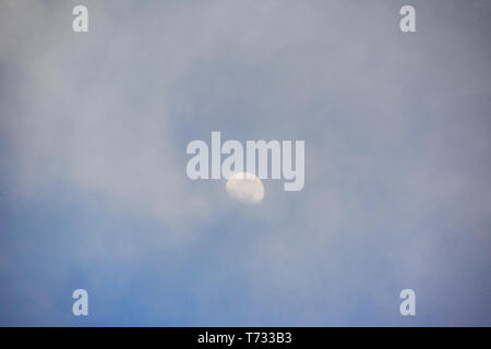 Moon during the day, partially hidden by mist and clouds Stock Photo