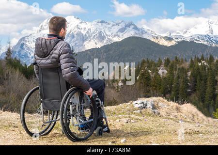 Young disabled man in wheelchair outside in nature observing mountains and nature Stock Photo