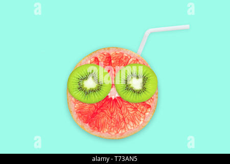 Fruit creative face with slices of grapefruit and kiwi, drinking straw on blue background, fruit juice and summer concept Stock Photo