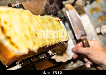 Raclette on the raclette grill is already grilled and spread with a knife on the bread and it smokes nicely Stock Photo