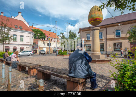 A man and two other people are sitting in a small square in which stands a sculpture of a decorated egg in Vilnius, Lithuania Stock Photo