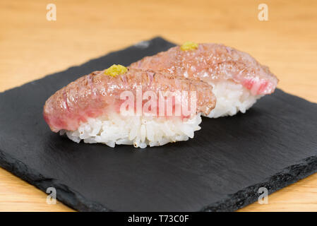 nigiri of heat-burned kobe beef dressed with mustard, served on a square plate of slate, wooden table background Stock Photo